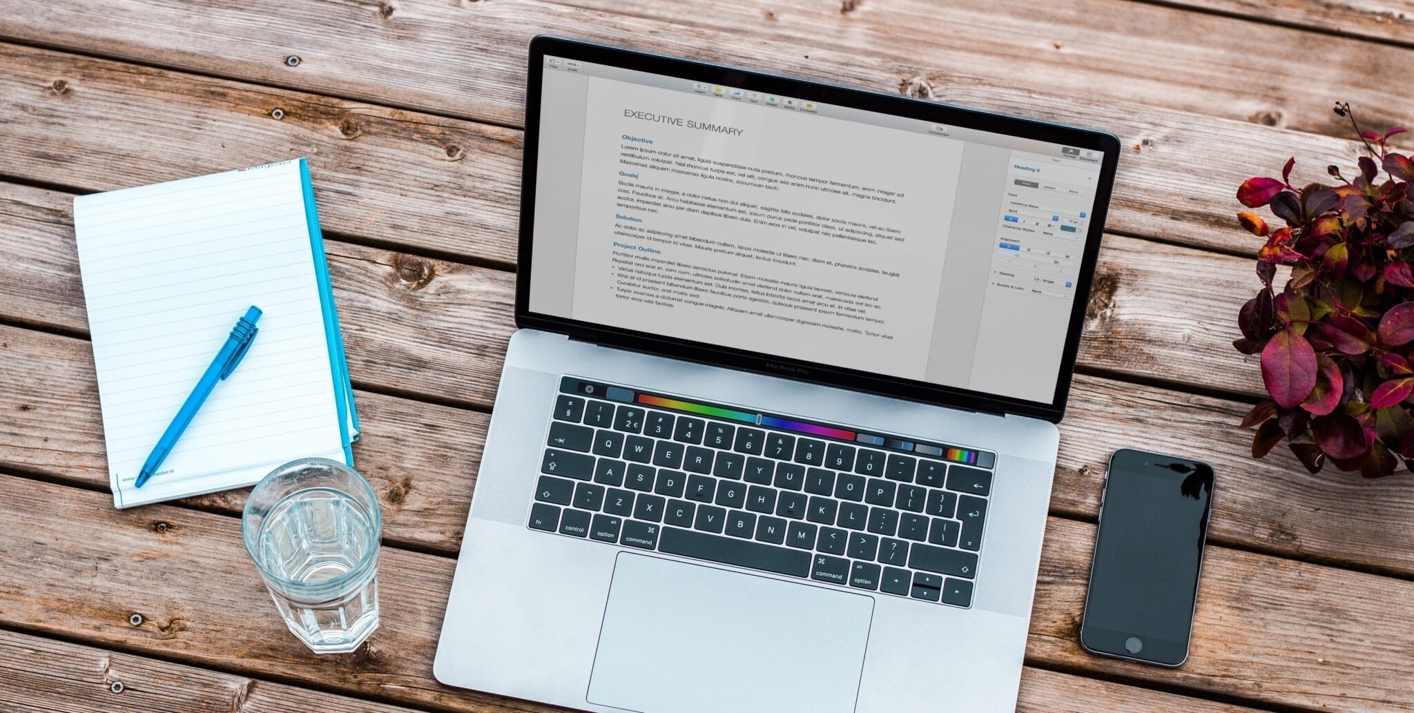 A desk with a laptop, notebook, pen, and a glass of water